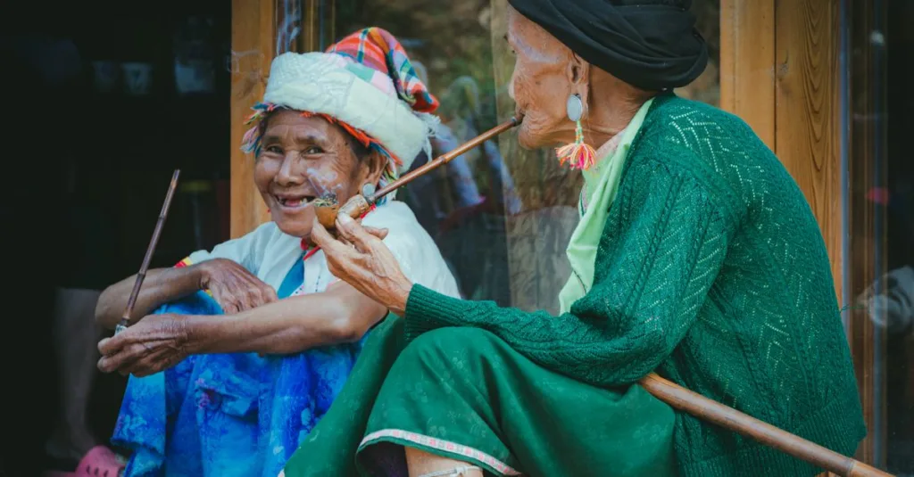 Dua wanita senior dalam pakaian tradisional menikmati momen ramah, merokok pipa panjang.