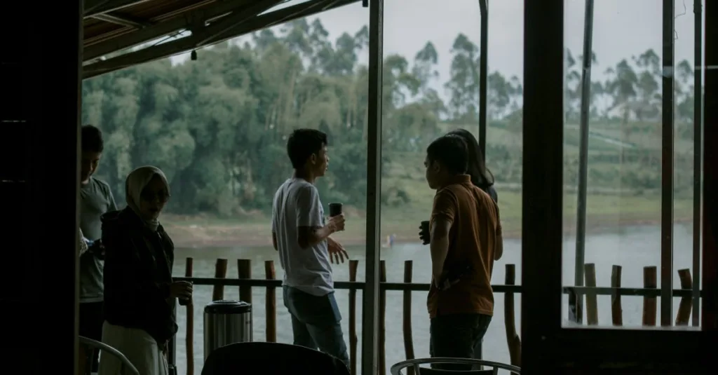 Sekelompok orang dewasa menikmati percakapan santai di teras tepi sungai, dengan latar belakang hijau subur.