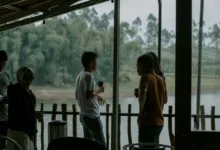 Sekelompok orang dewasa menikmati percakapan santai di teras tepi sungai, dengan latar belakang hijau subur.