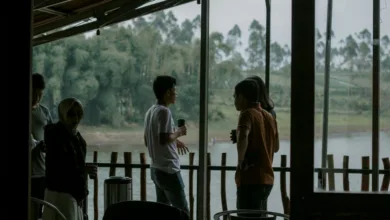Sekelompok orang dewasa menikmati percakapan santai di teras tepi sungai, dengan latar belakang hijau subur.