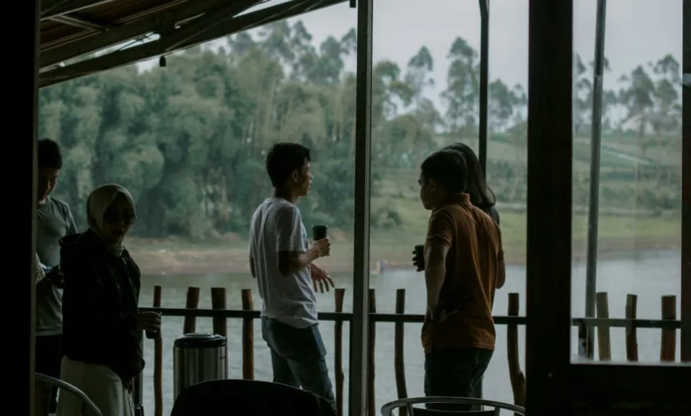 Sekelompok orang dewasa menikmati percakapan santai di teras tepi sungai, dengan latar belakang hijau subur.
