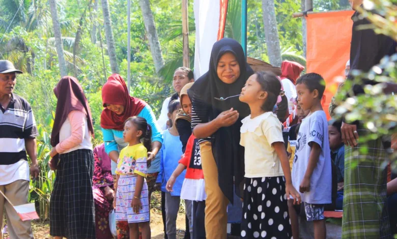 Pertemuan luar ruangan yang meriah dengan anak-anak dan orang dewasa berinteraksi di bawah sinar matahari dekat pohon.
