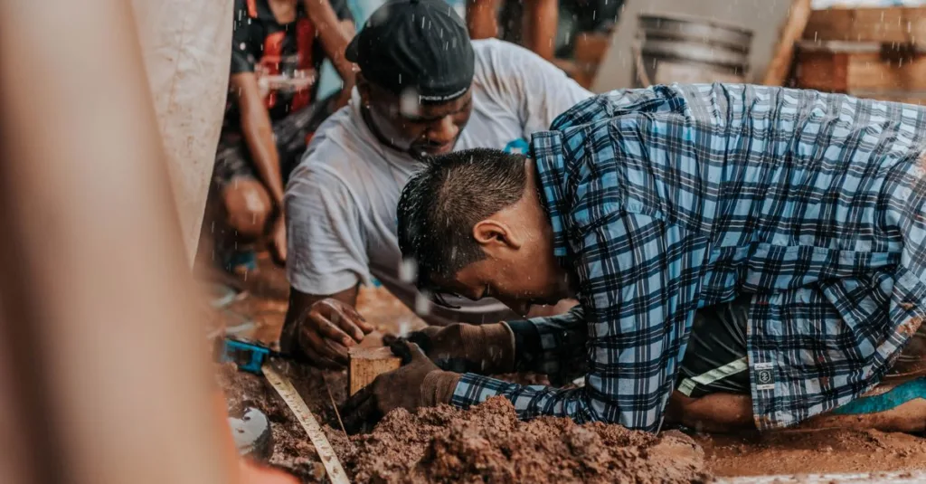 Sekelompok pria berkolaborasi dalam proyek konstruksi di luar ruangan dengan nuansa earthy.