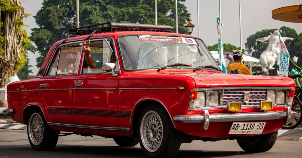 Sedan merah klasik dipamerkan di acara mobil luar ruangan, menonjolkan gaya otomotif vintage.