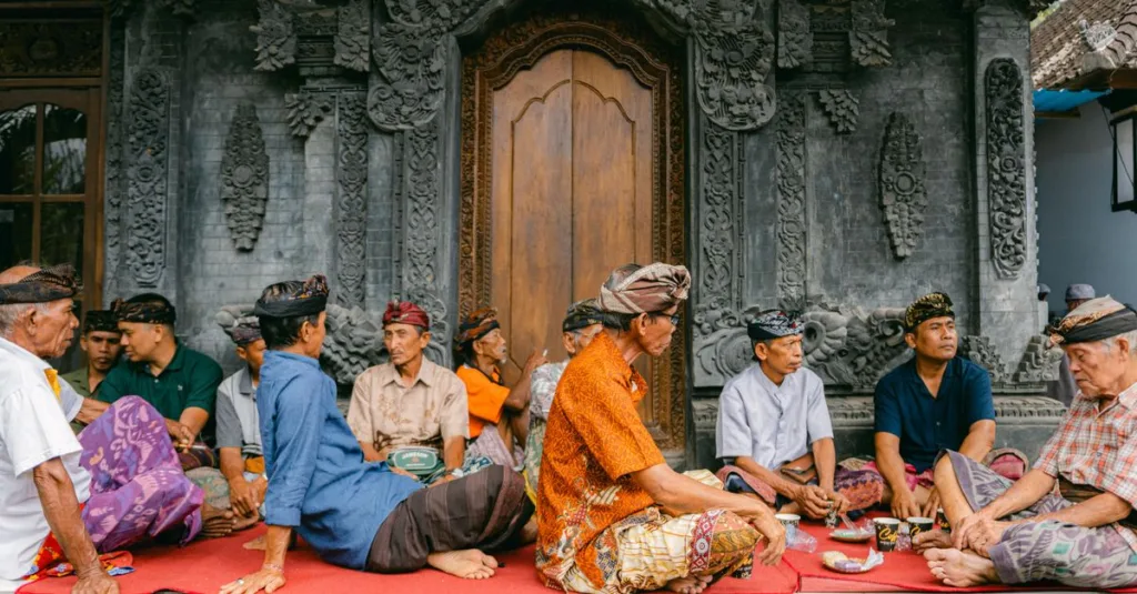 Sekelompok pria berpakaian tradisional duduk di luar pura Bali, asyik mengobrol.