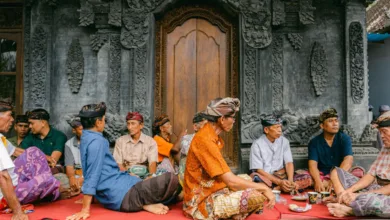 Sekelompok pria berpakaian tradisional duduk di luar pura Bali, asyik mengobrol.