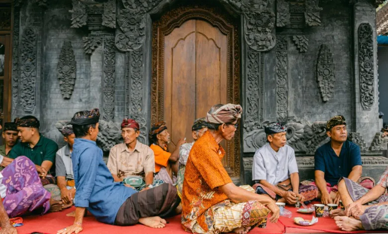 Sekelompok pria berpakaian tradisional duduk di luar pura Bali, asyik mengobrol.