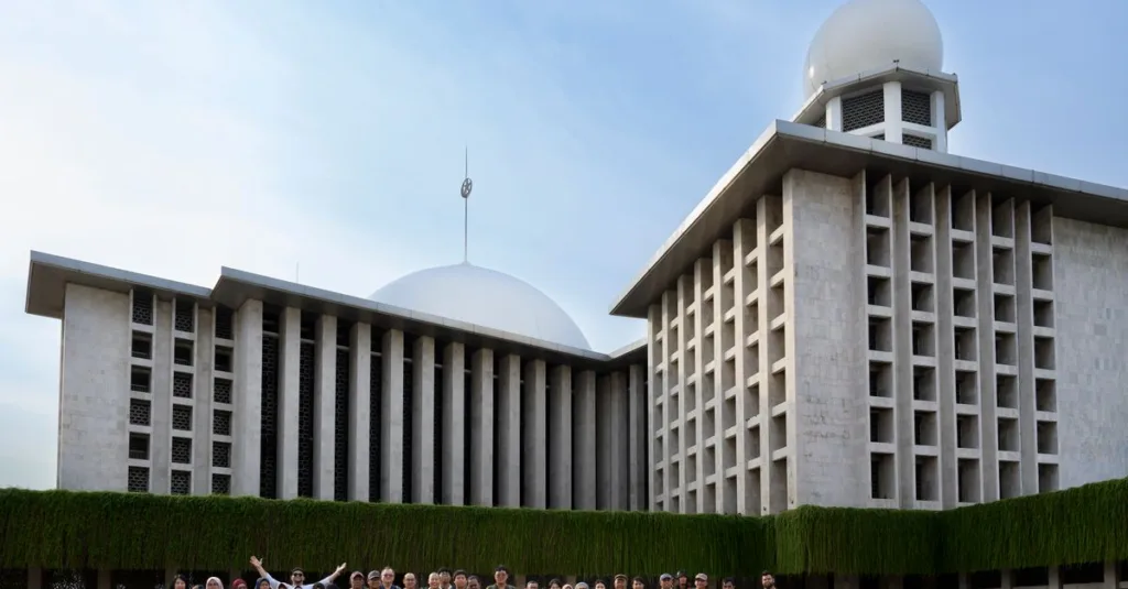 Sekelompok orang yang beragam berpose di luar Masjid Istiqlal yang ikonik di Jakarta, memamerkan arsitekturnya yang unik.