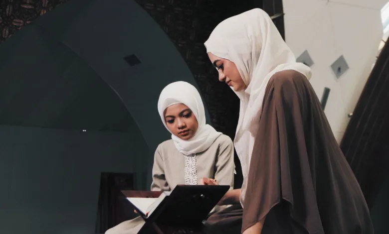 Dua wanita Muslim membaca Al-Qur'an di lingkungan masjid yang tenang di Bandung, Indonesia.