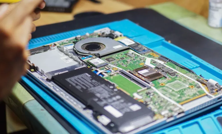 Tampilan dekat laptop yang sedang diperbaiki dengan komponen dan peralatan yang terlihat.