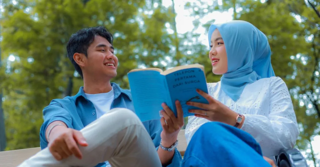 Sepasang kekasih muda menikmati membaca buku bersama di taman Jakarta yang cerah.