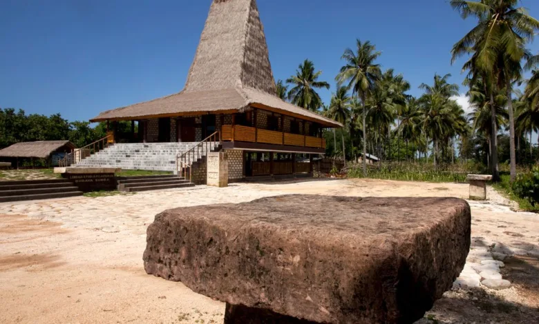 Jelajahi rumah tradisional Sumbawa yang dikelilingi pohon palem rimbun di bawah langit biru cerah.