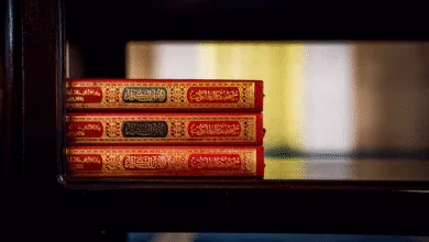 Tiga Quran dengan sampul yang ornamen dipajang di rak kayu di dalam masjid, menyoroti budaya Islam.