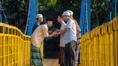 Laki-laki berpakaian tradisional saling menyapa dengan hangat di jembatan gantung di Jawa Barat, Indonesia.