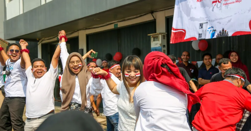 Perayaan luar ruangan yang penuh kegembiraan untuk Hari Kemerdekaan Indonesia dengan orang-orang yang bermain permainan tradisional.