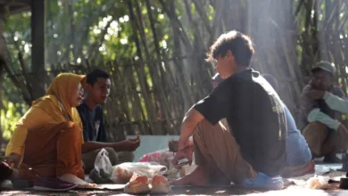 Sekelompok orang berkumpul di luar ruangan di alam, terlibat dalam percakapan dan berbagi makanan.