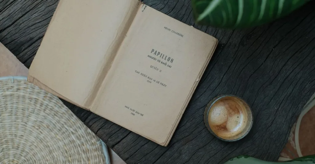 Buku terbuka 'Papillon' dengan kopi di pengaturan meja rustic, membangkitkan suasana vintage dan nyaman.