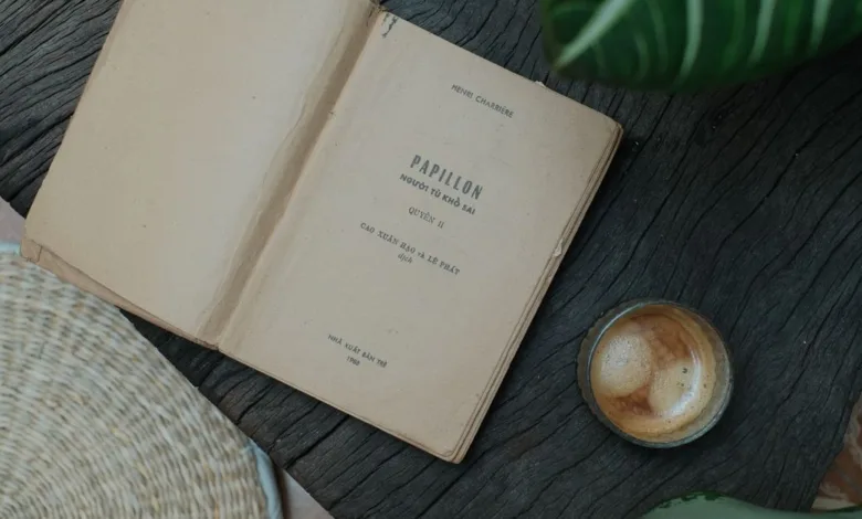 Buku terbuka 'Papillon' dengan kopi di pengaturan meja rustic, membangkitkan suasana vintage dan nyaman.
