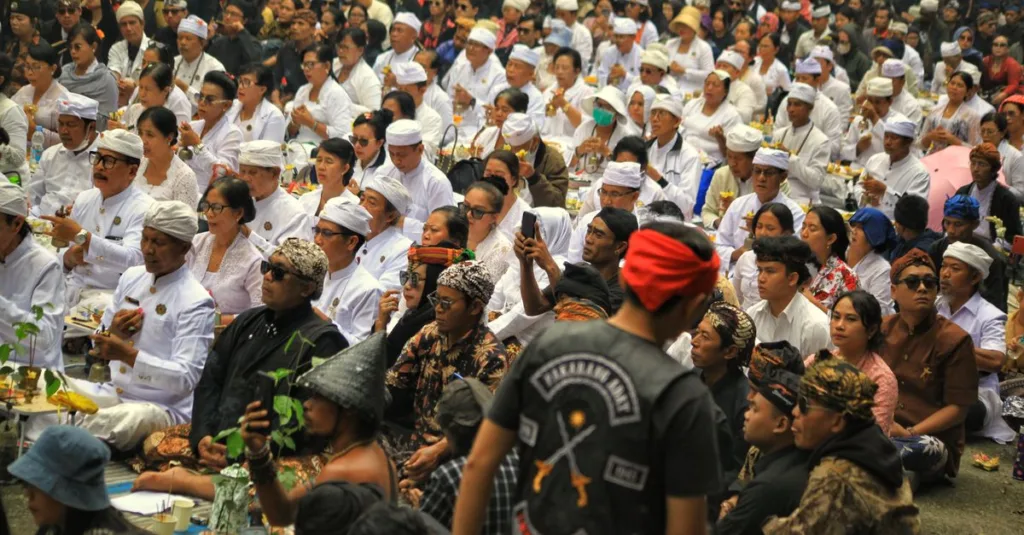 Sekumpulan besar orang mengenakan pakaian tradisional menghadiri upacara keagamaan di luar ruangan di Jawa Barat, Indonesia.
