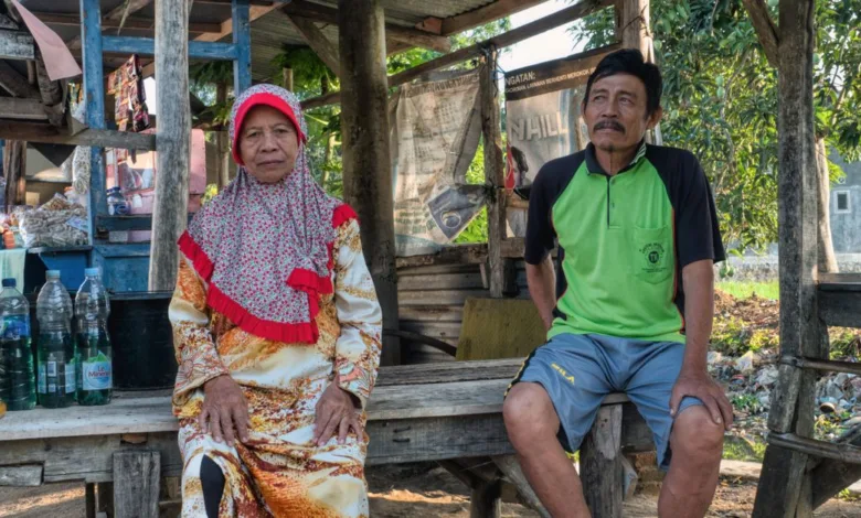 Pasangan lansia duduk di luar ruangan dalam suasana desa Indonesia yang rustic, mencerminkan gaya hidup yang damai.