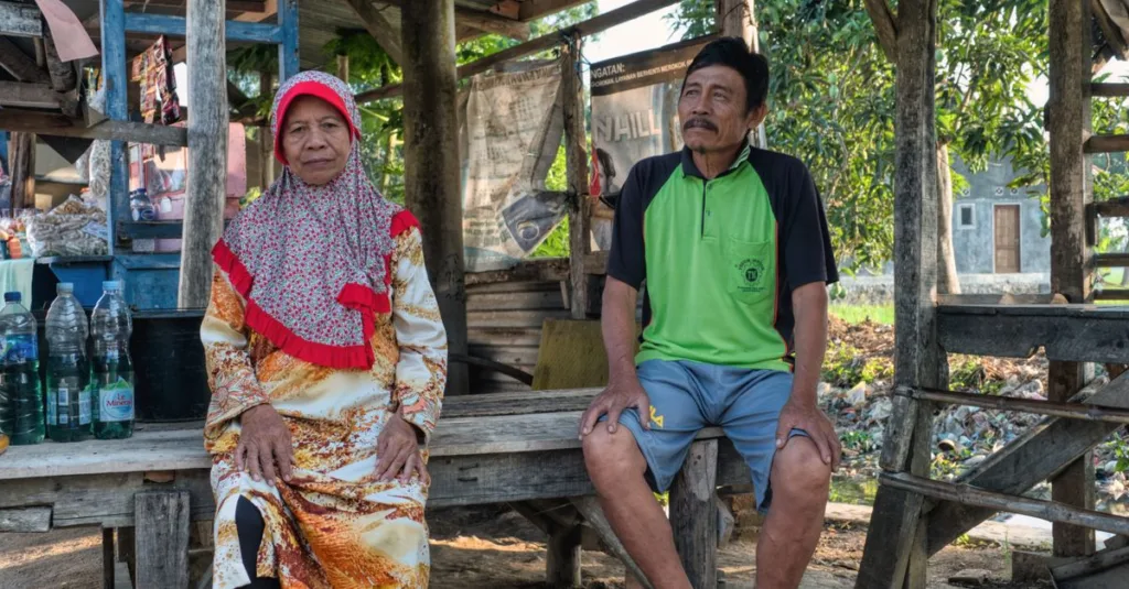 Sepasang suami istri tua bersantai di luar ruangan di sebuah desa di Jawa Barat, mengenakan pakaian tradisional.
