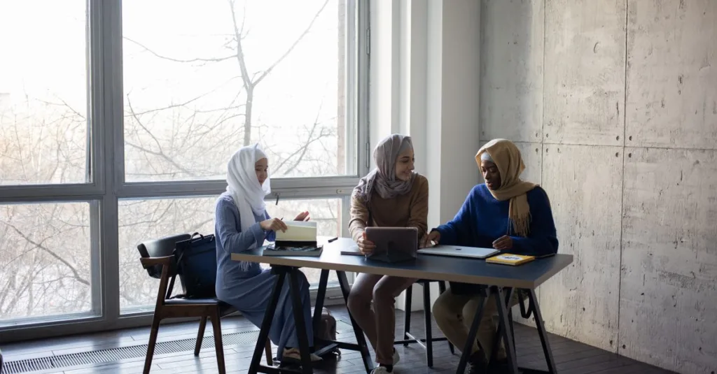Tiga wanita Muslim berjilbab berkolaborasi di meja kantor modern.