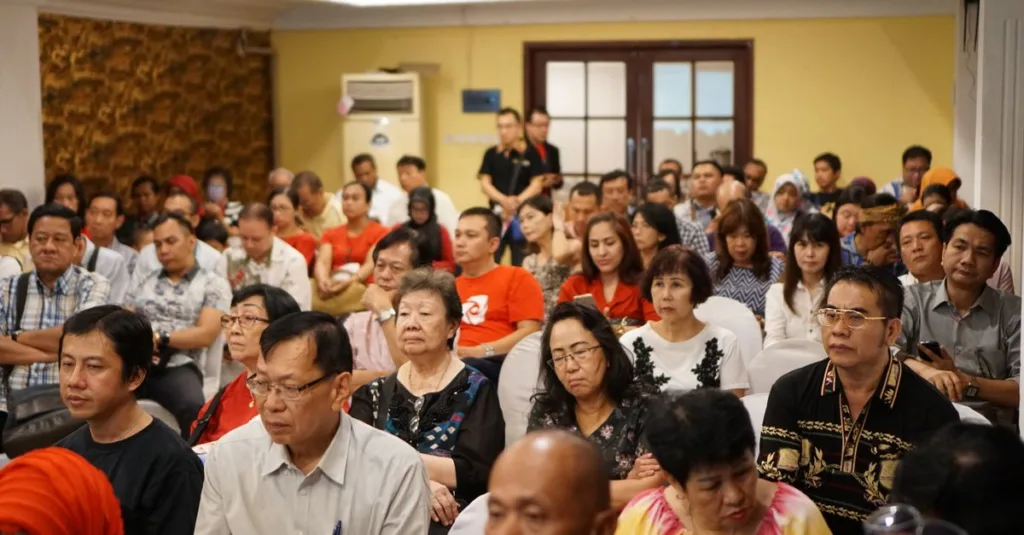Sekelompok orang dewasa yang beragam menghadiri konferensi di sebuah pengaturan dalam ruangan di Indonesia.